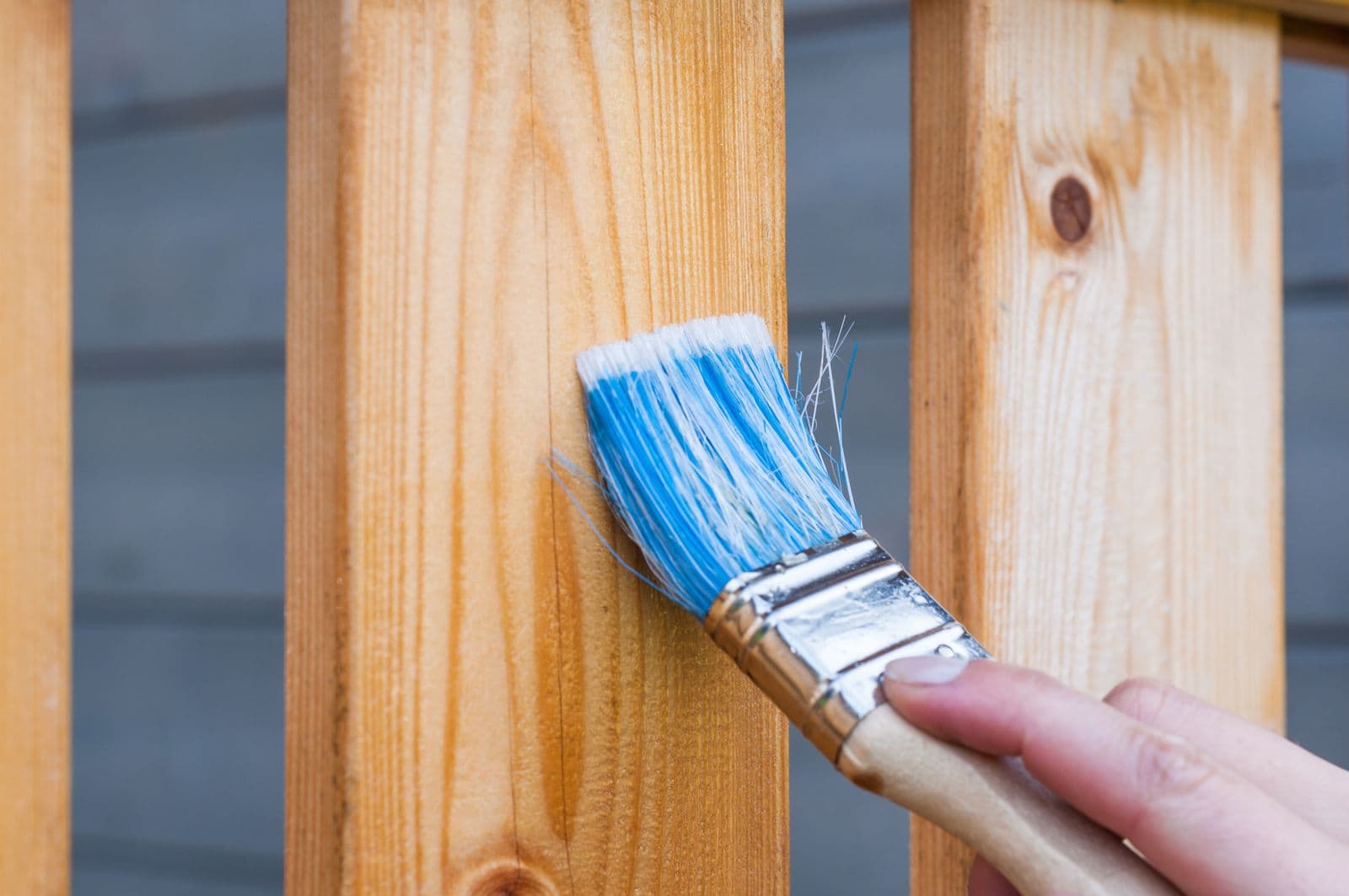 Hand brushing blue paint onto a wooden fence plank